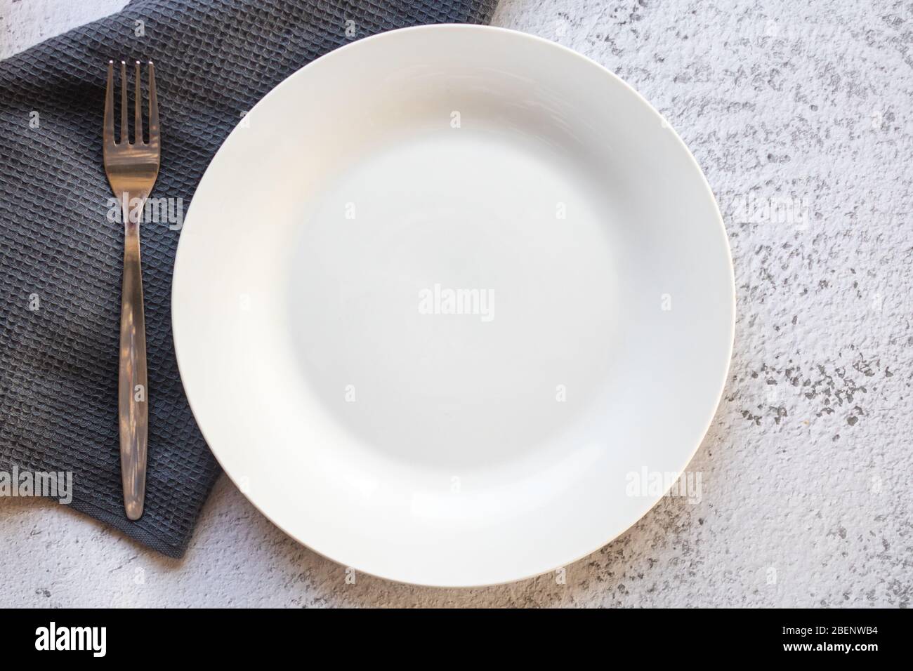 Empty white plate next to a gray kitchen towel Stock Photo