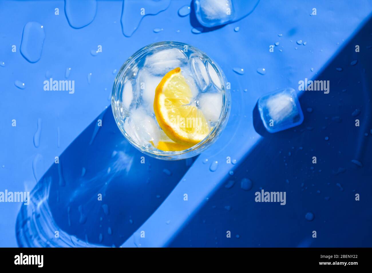 A glass of refreshing water with ice and lemon on a blue background. Heat concept, fresh. Natural light. Flat lay, top view, copy space Stock Photo