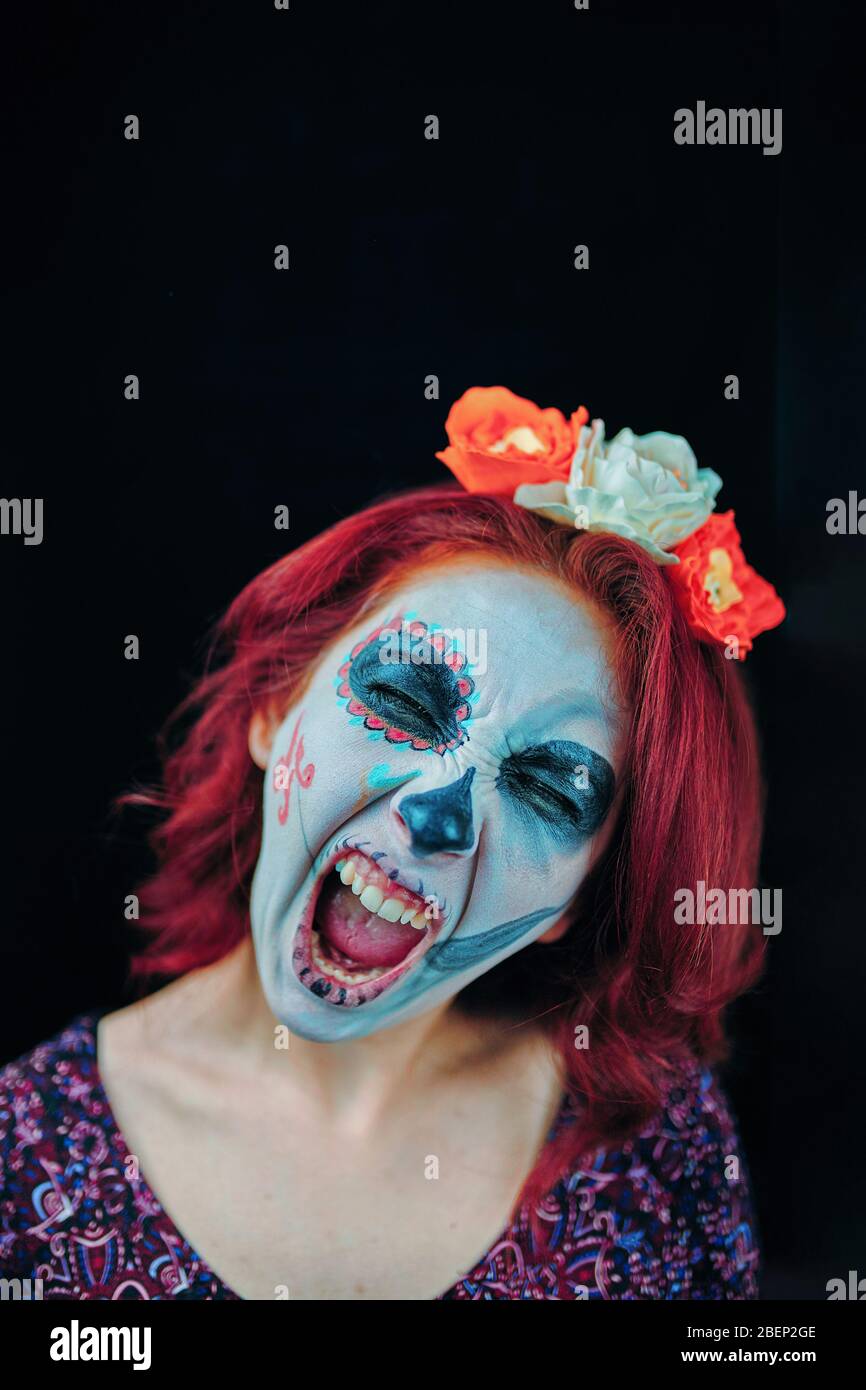 Young woman in day of the dead mask skull face art and red hair, screaming on dark background Stock Photo