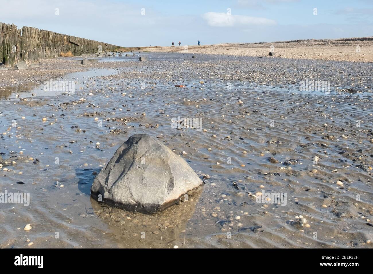 A soothing picture of the wadden sea at paesens moddergat, big rock in foreground, sea and sky, people in the distance. Stock Photo