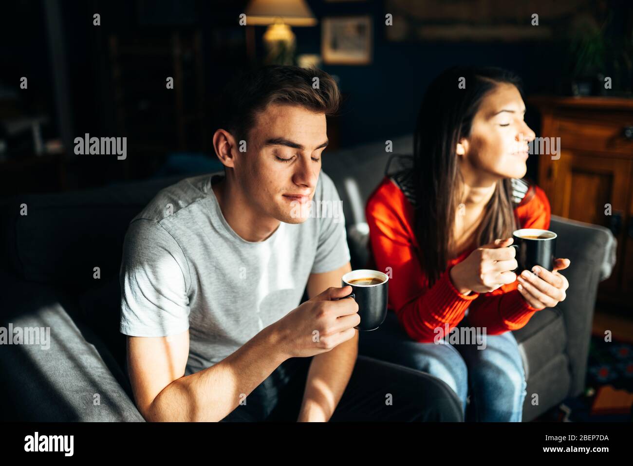 Young couple staying at home,drinking coffee at the window.Enjoying view,sun rays.Serene mornings.Family avoiding social contact.Quaratine Stock Photo