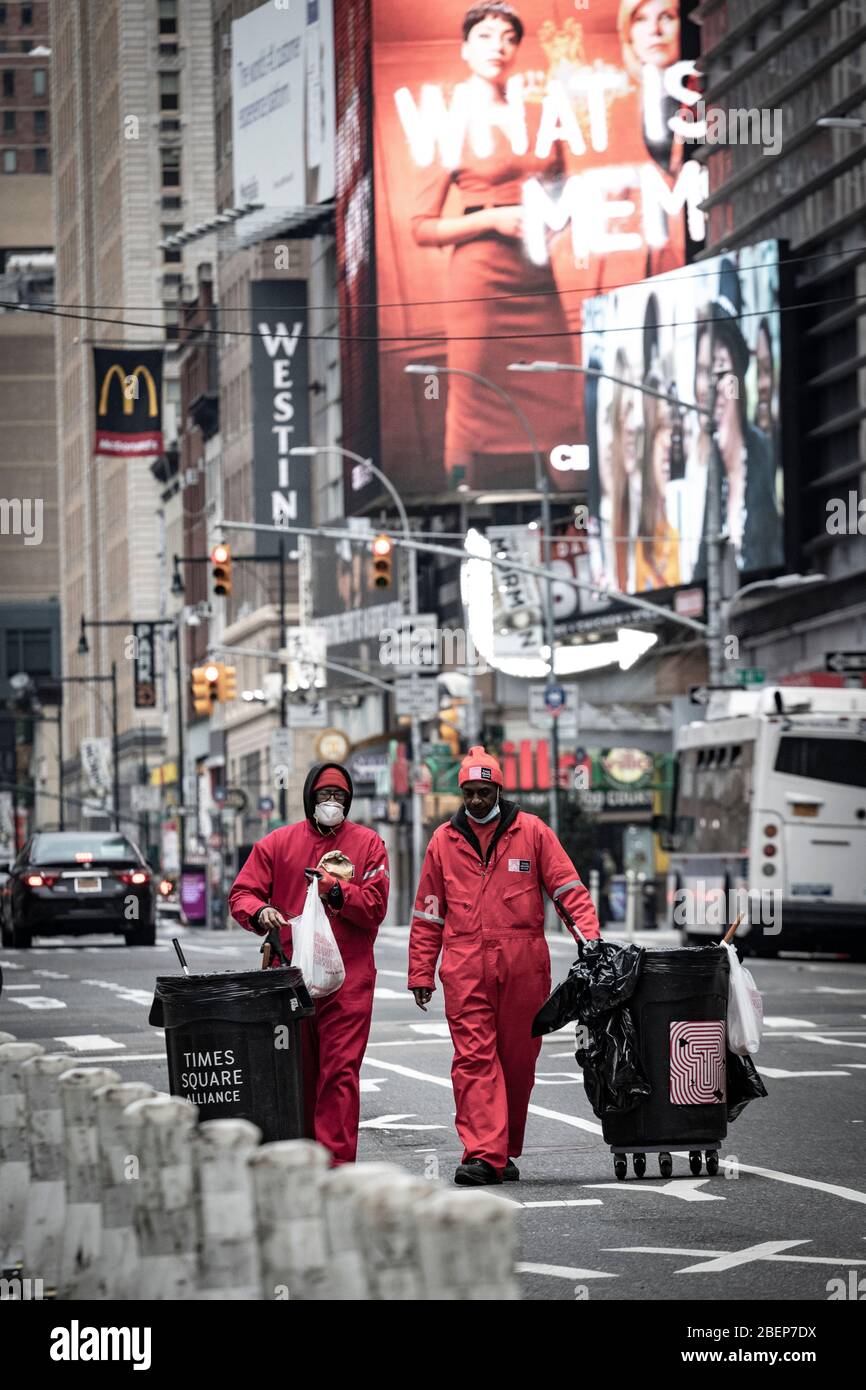 Sanitation workers in Times Square area streets, cleaning litter in city on foot with rolling trash cans and in red uniforms. Stock Photo