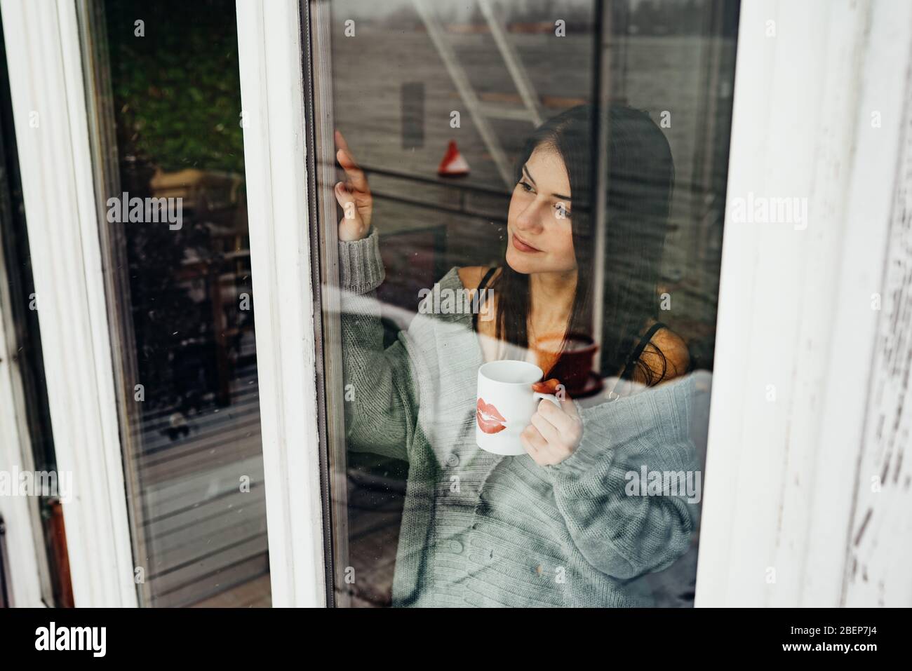 Young woman spending free time home.Self care,staying home.Enjoying view,gazing through to the window.Quarantined person indoors. Stock Photo