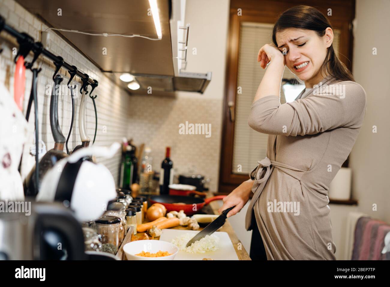Young housewife beginner cook crying while cutting onion.Slice,dice and chop onion.Stinging eyes and tears when cutting onions to prepare dinner.Shedd Stock Photo
