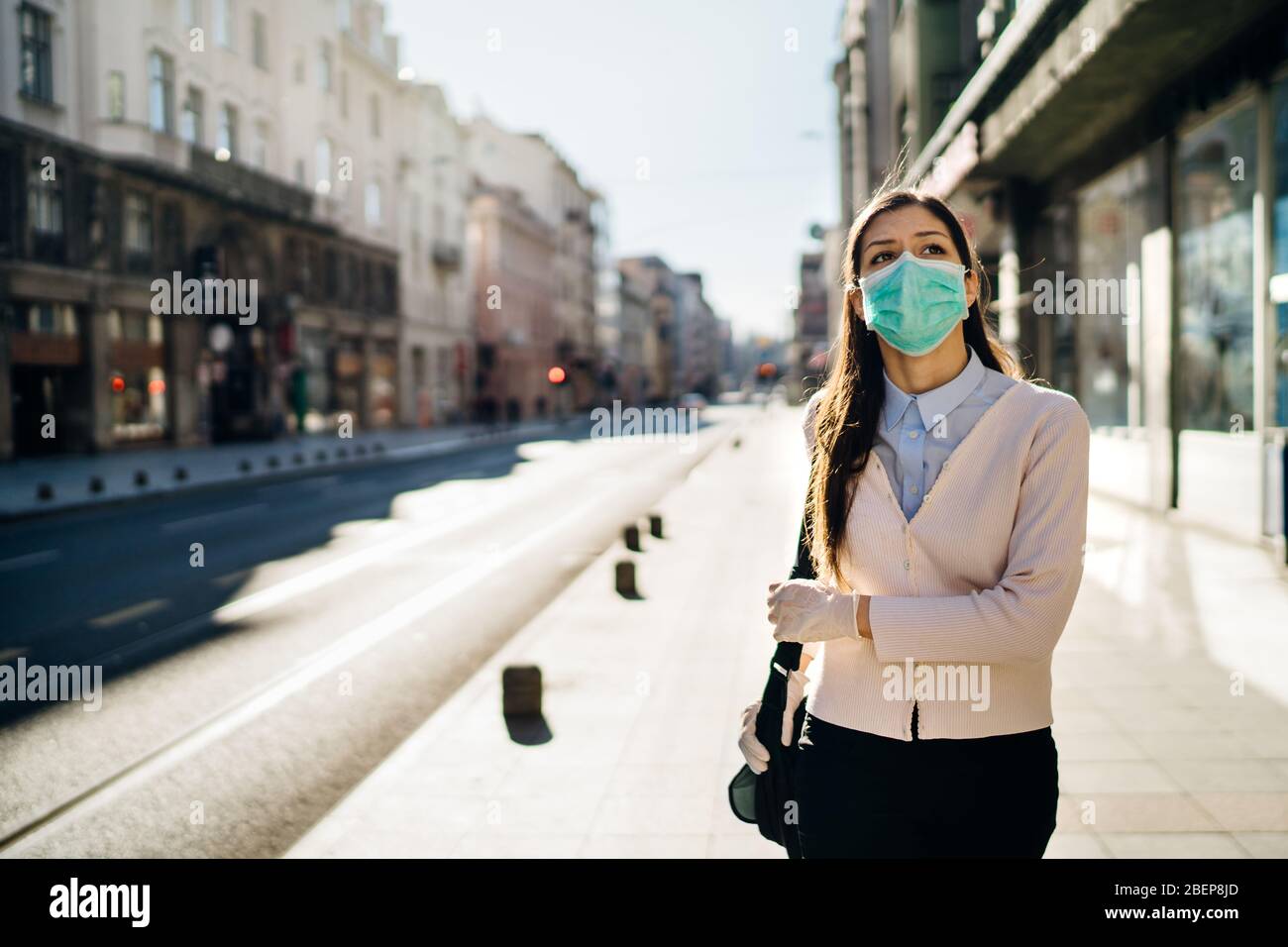 Concerned woman walking to work in public space during pandemic.Effect of the COVID-19.Protective measure,mask wearing.Respecting guidelines.Empty str Stock Photo