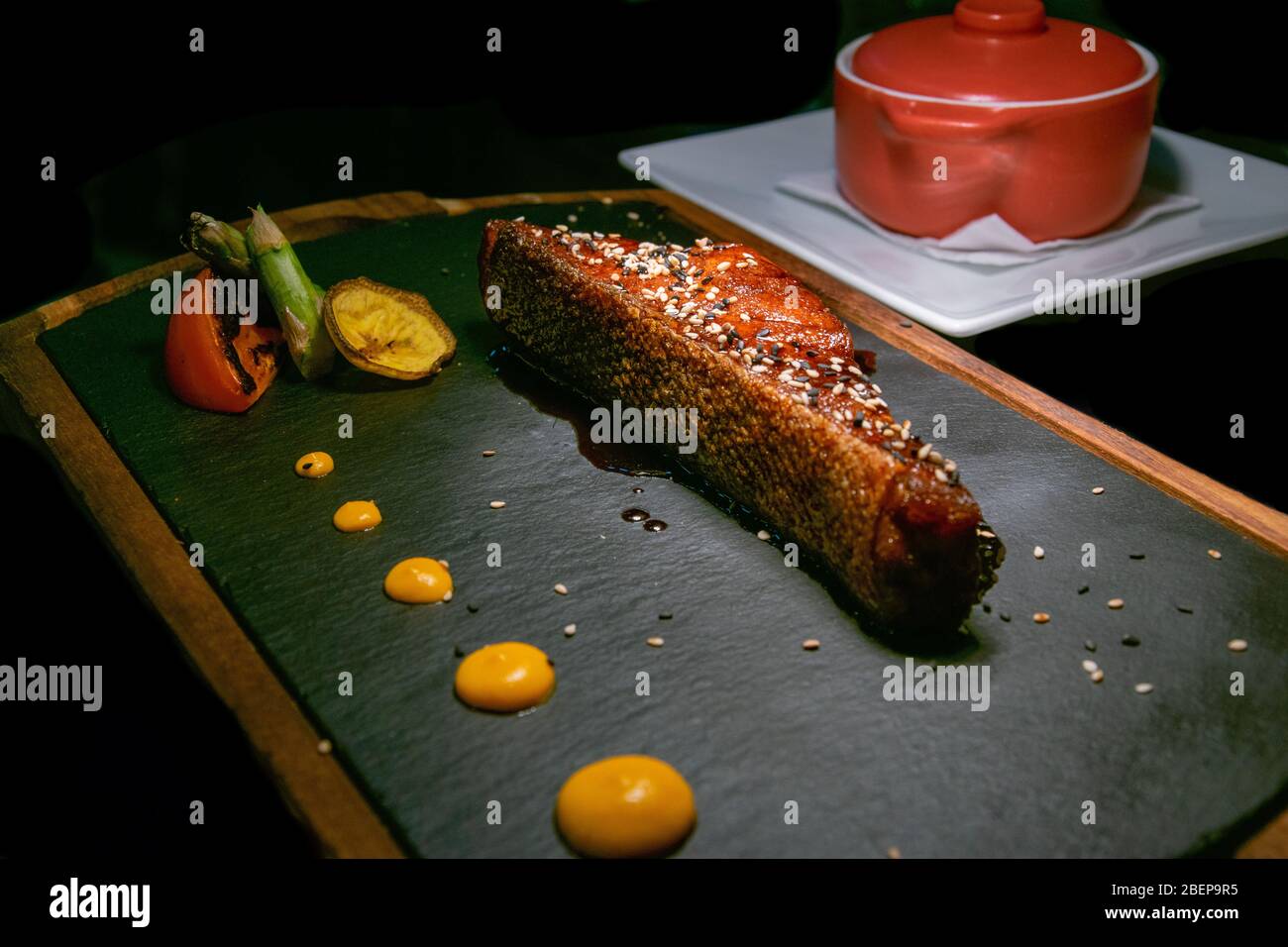 a piece of Canadian salmon cooked in a teriyaki sauce served on a stone and wood plate alongside a side dish of steamed rice Stock Photo