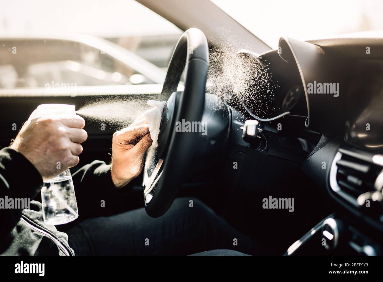 Car owner disinfecting vehicle with alcohol based sanitizing solution spray.Touched surfaces sanitation.Coronavirus COVID-19 spread prevention.Cross-c Stock Photo
