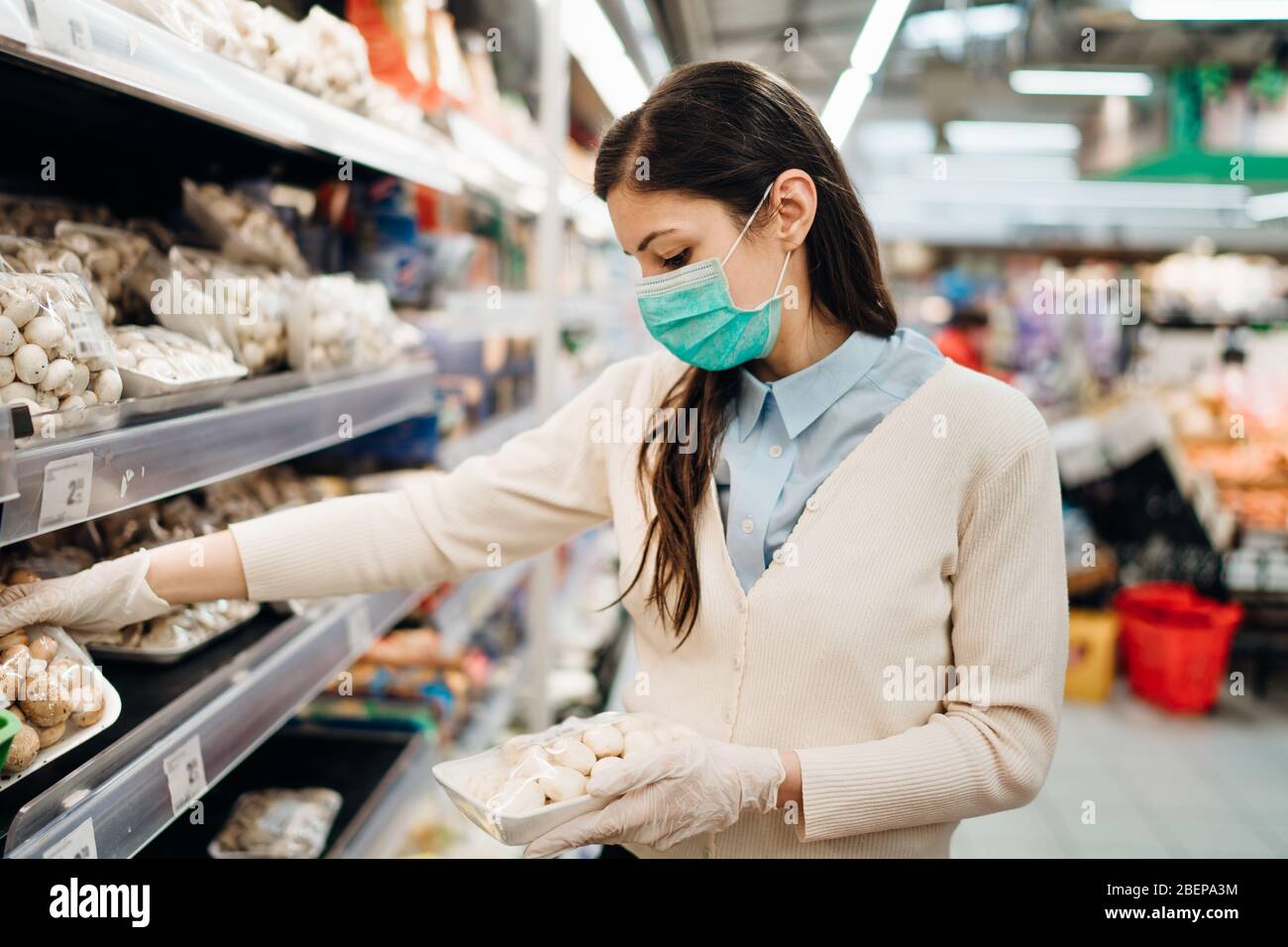 Woman with mask safely shopping for groceries amid the coronavirus pandemic in a stocked grocery store.COVID-19 food buying in supermarket.Panic buyin Stock Photo
