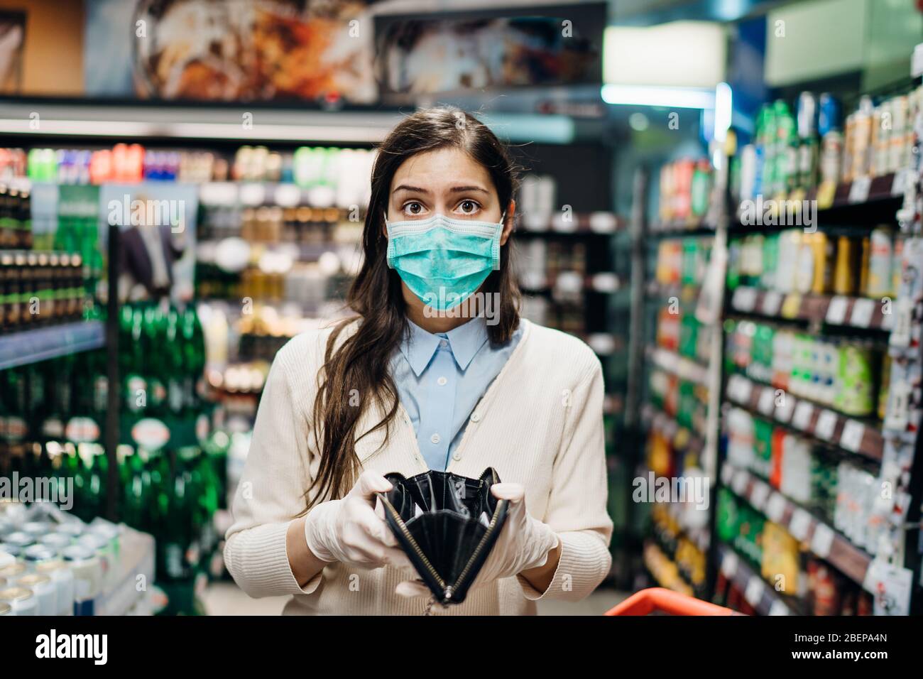 Stressed woman with mask shopping in grocery store with an empty wallet.Bankruptcy/recession.Covid-19 quarantine lockdown impact.Unemployed person in Stock Photo