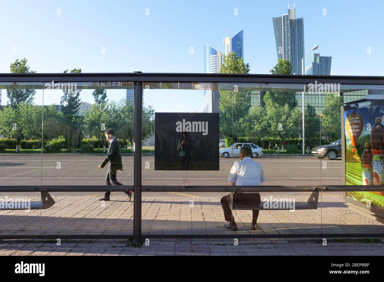 NUR-SULTAN, ASTANA, KAZAKHSTAN - JUNE 3, 2015: A bus stop vith sunny city view with skyscapers and several people around. Reflection of photographer Stock Photo