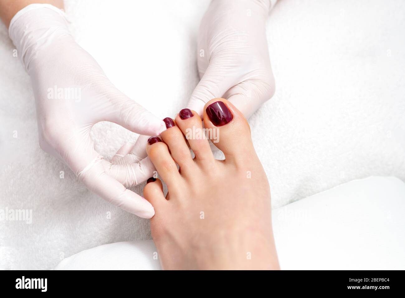 Pedicurist hands showing woman toenails painted in dark red color, top view. Stock Photo
