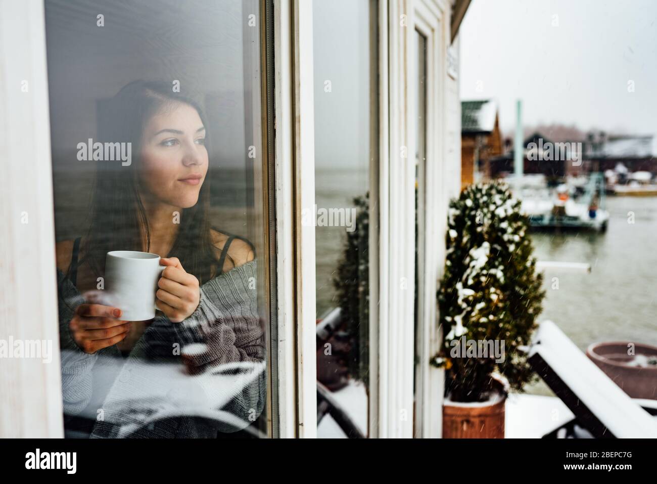 Young woman spending free time home.Self care,staying home.Enjoying view,gazing through to the window.Quarantined person indoors.Serene mornings. Stock Photo