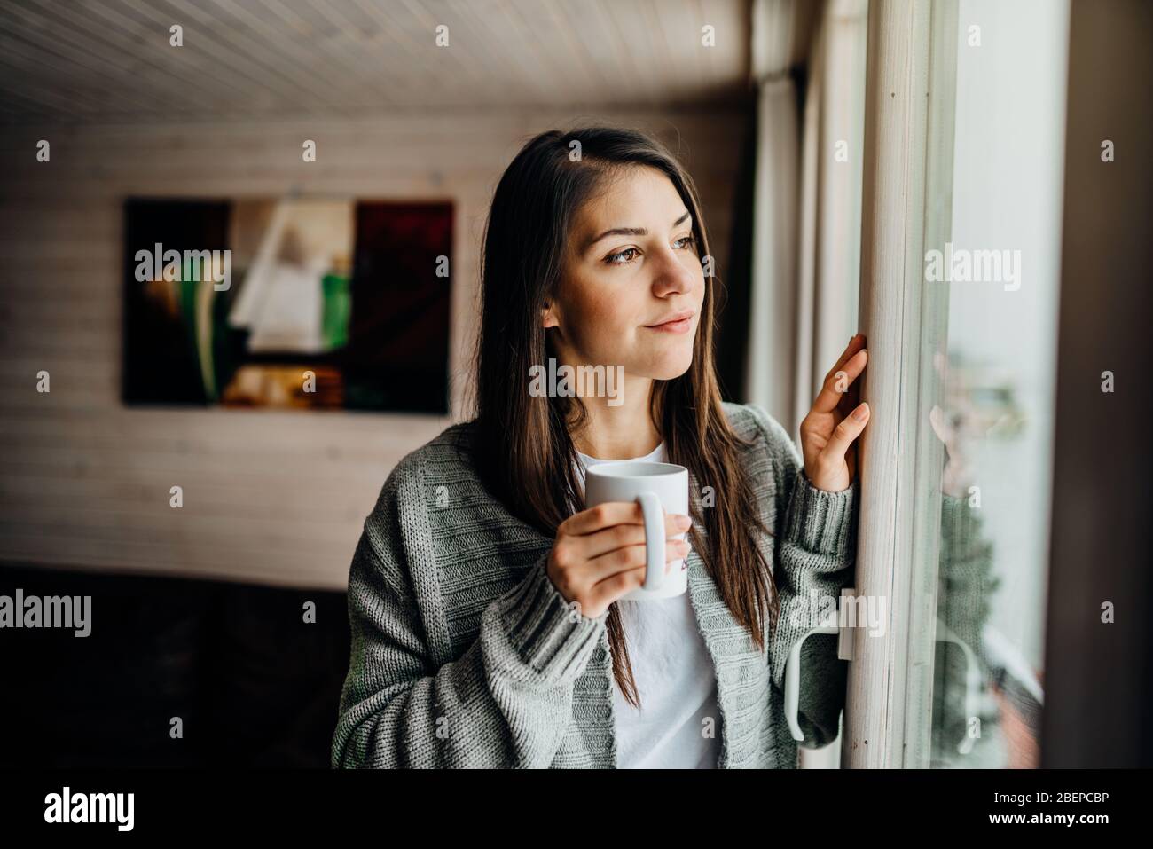 Young woman spending free time home.Self care,staying home.Enjoying view,gazing through to the window.Quarantined person indoors.Serene mornings.Avoid Stock Photo