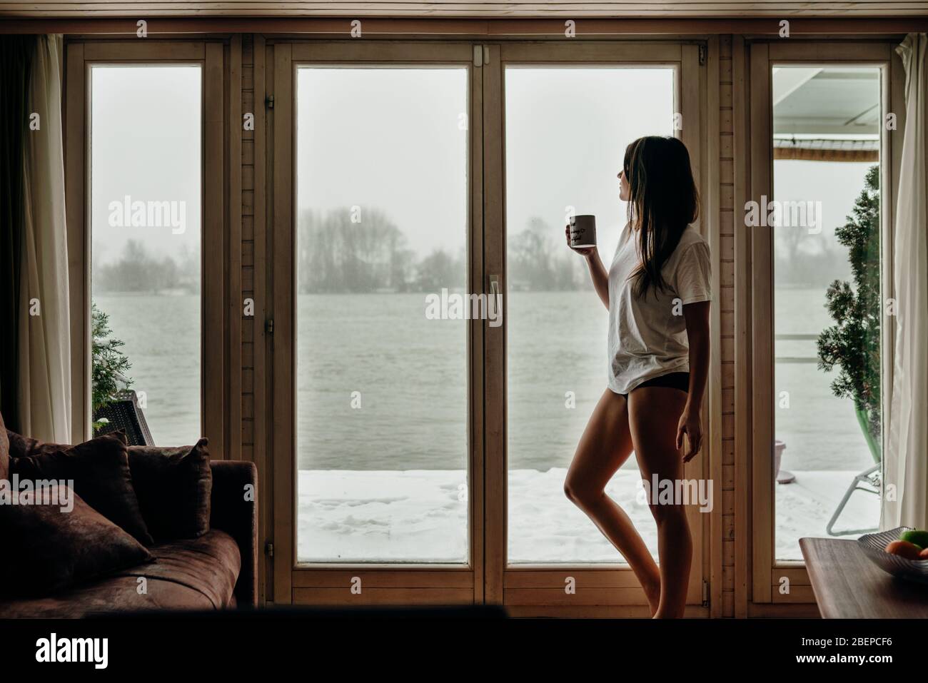 Young woman spending free time home.Self care,staying home.Enjoying view,gazing through to the window.Quarantined person indoors.Serene mornings.Avoid Stock Photo