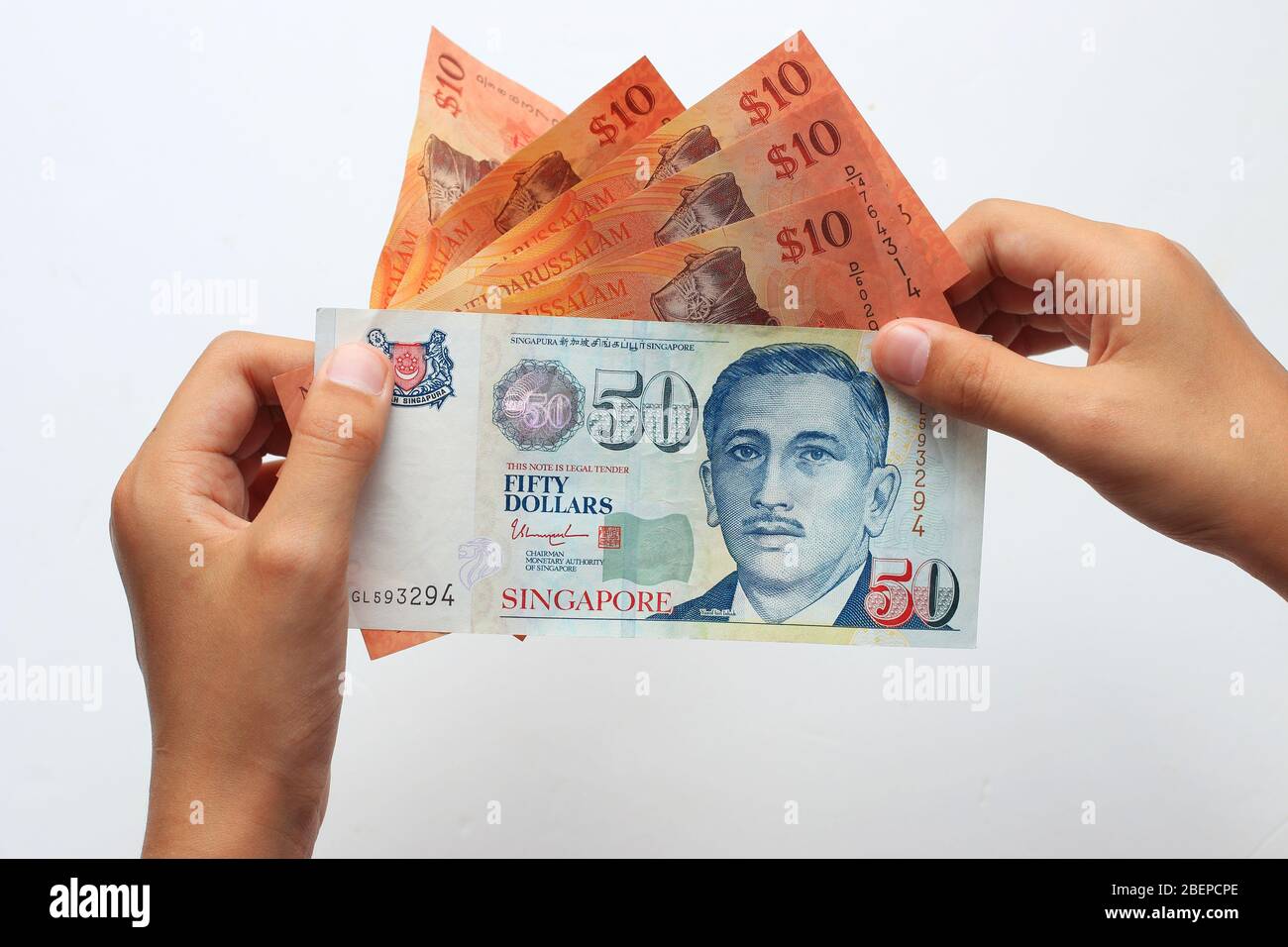 Hand holding Singaporean $50 and Brunei $10 currencies isolated against white background Stock Photo