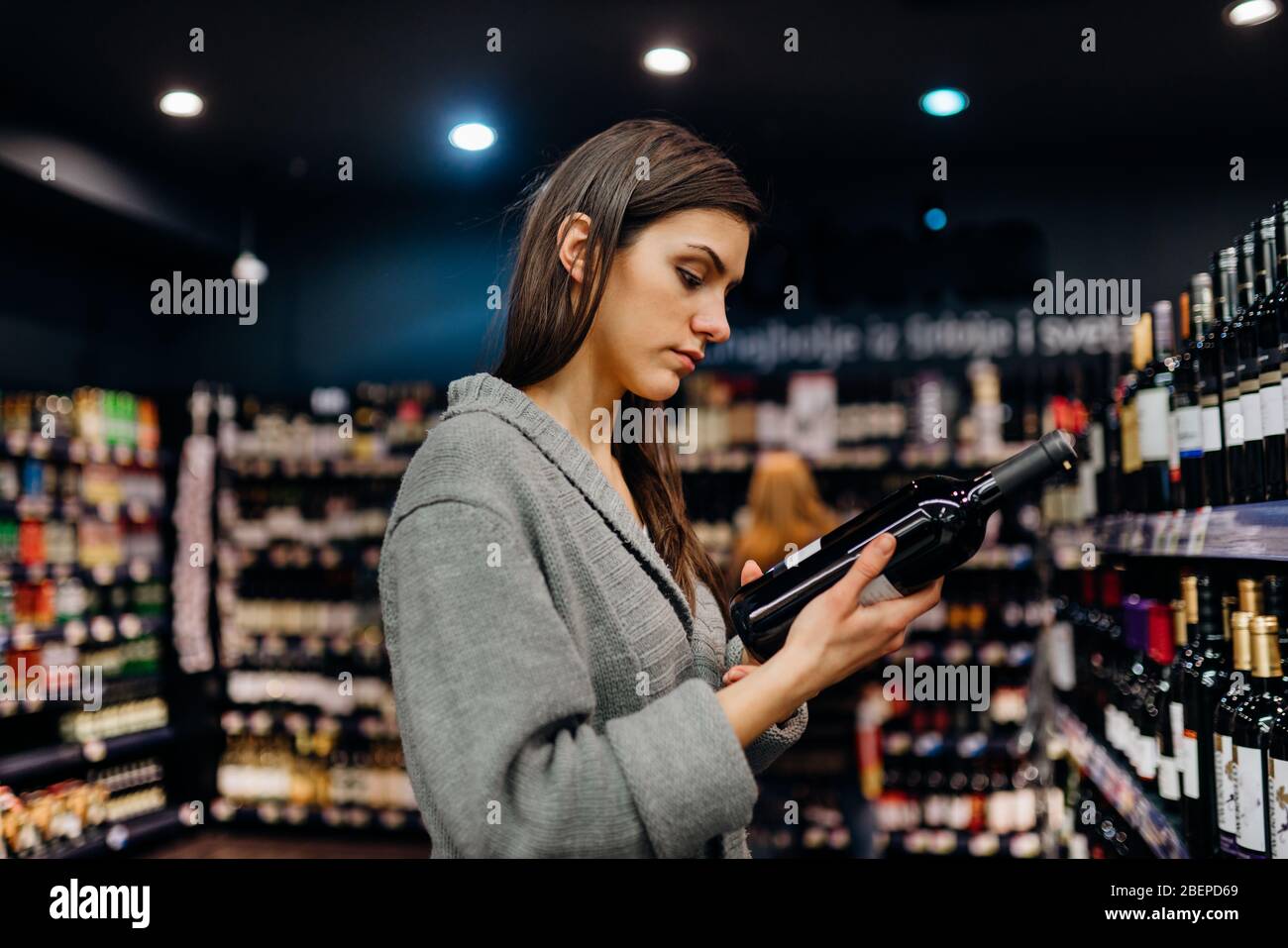 Woman shopping for expensive wine in supermarket alcohol store.Choosing and buying good cheap wine.Benefits of drinking wine.Resveratrol.Everyday bing Stock Photo