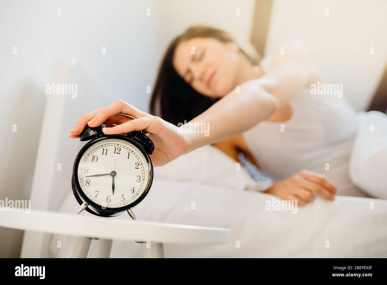 Alarm clock ringing,annoyed woman waking up in early morning for work.Sleeping disorder.Tired woman oversleeping,bad sleep quality.Sleep deprived.Bad Stock Photo
