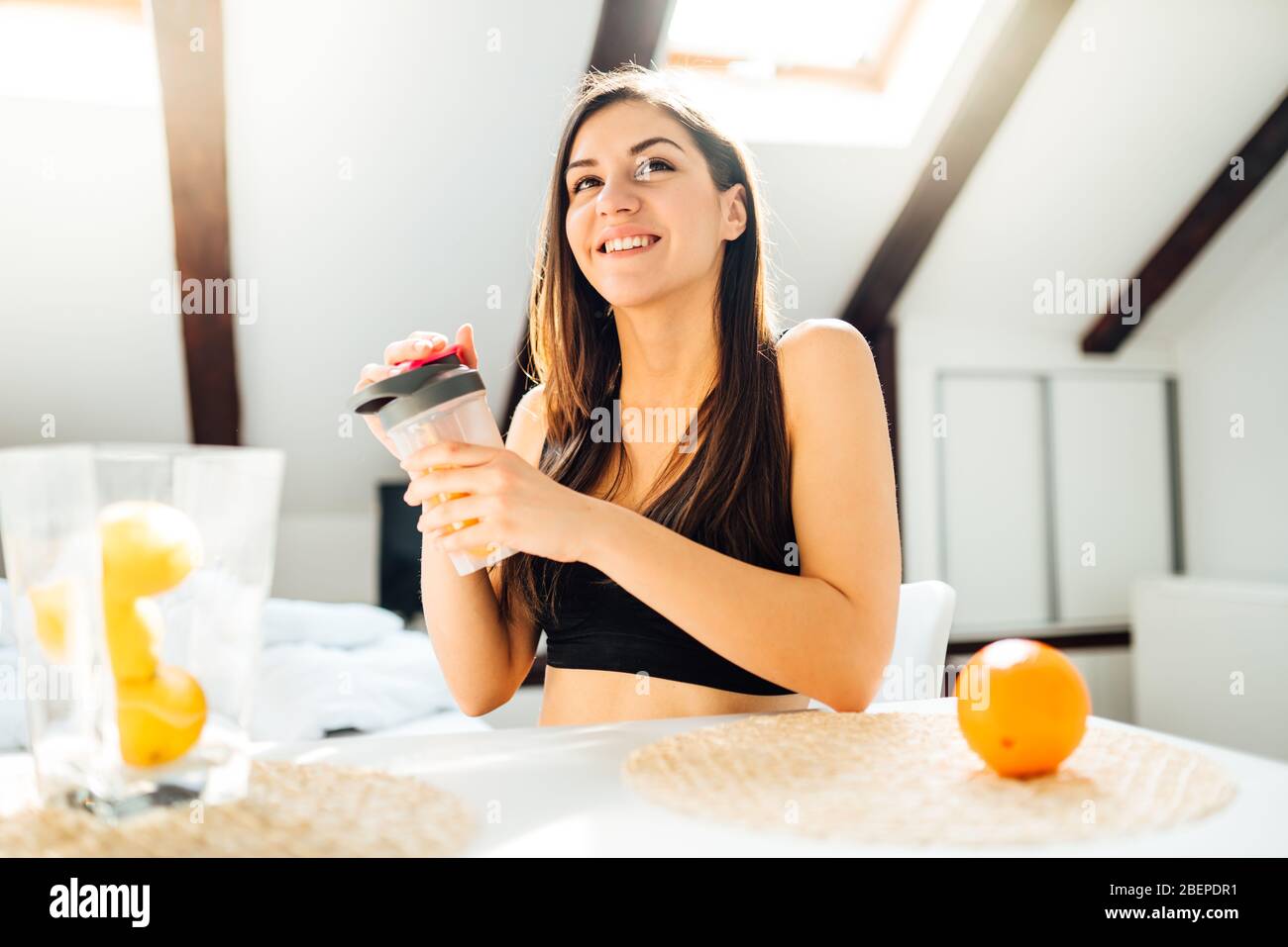 Healthy woman in sportswear drinking sweet orange juice smoothie after home workout.Vitamin supplement.After exercise shaker meal.Weight loss fitness Stock Photo