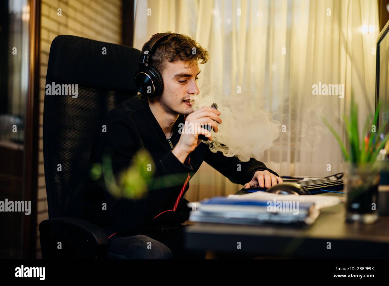 Young man gamer inhaling of a vapor with electronic cigarette.Vape flavor liquid chemicals.Use of e-cigarettes in the home.Smoking and vaping negative Stock Photo