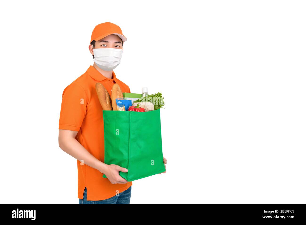 Hygienic man wearing medical mask carrying supermarket grocery shopping bag offering home delivery service isolated in white background Stock Photo