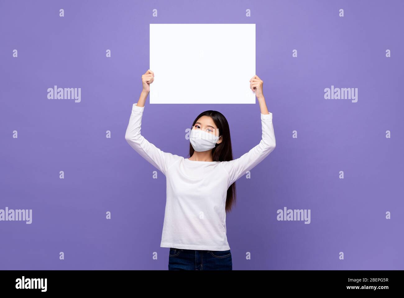 Young Asian woman wearing medical mask holding white paper board with empty space for text overhead Stock Photo