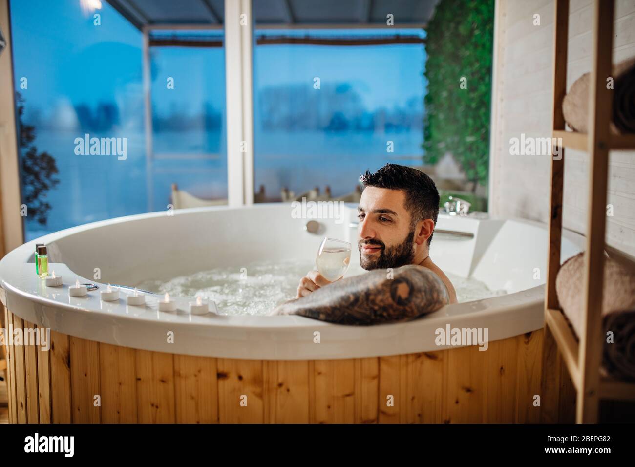 Man relaxing at home in the hot tub bath ritual with a glass of wine.Spa day moment in bathroom indoors jacuzzi tub.Leisure activity.Good personal hyg Stock Photo