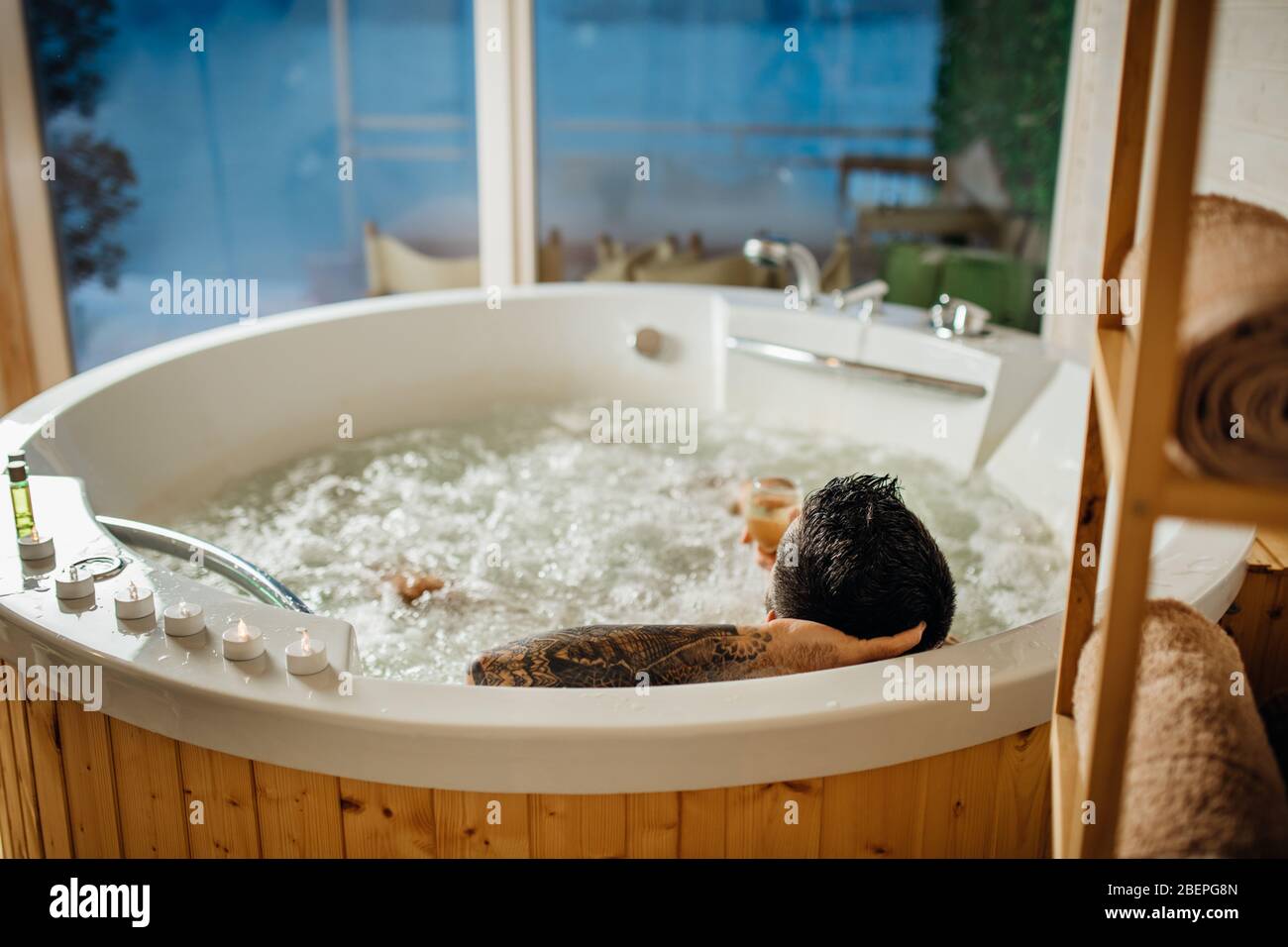 Man relaxing at home in the hot tub bath ritual with a glass of wine.Spa day moment in bathroom indoors jacuzzi tub.Leisure activity.Good personal hyg Stock Photo