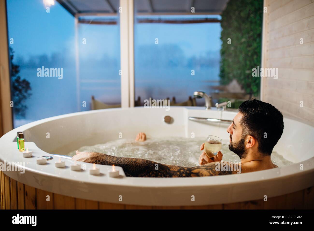Man relaxing at home in the hot tub bath ritual with a glass of wine.Spa day moment in bathroom indoors jacuzzi tub.Leisure activity.Good personal hyg Stock Photo