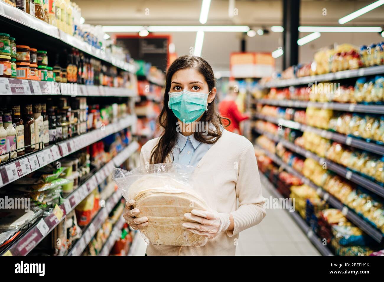 Scared shopper with mask safely shopping for groceries amid the coronavirus pandemic in stocked grocery store.COVID-19 food supermarket buying.Panic b Stock Photo