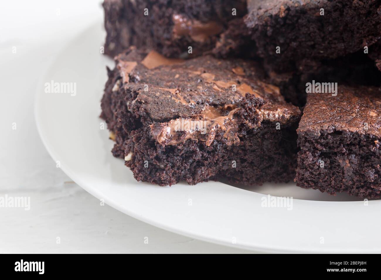 Chocolate brownies with melted chocolate bits stacked in a white plate  on white rustic background close up with space for text Stock Photo