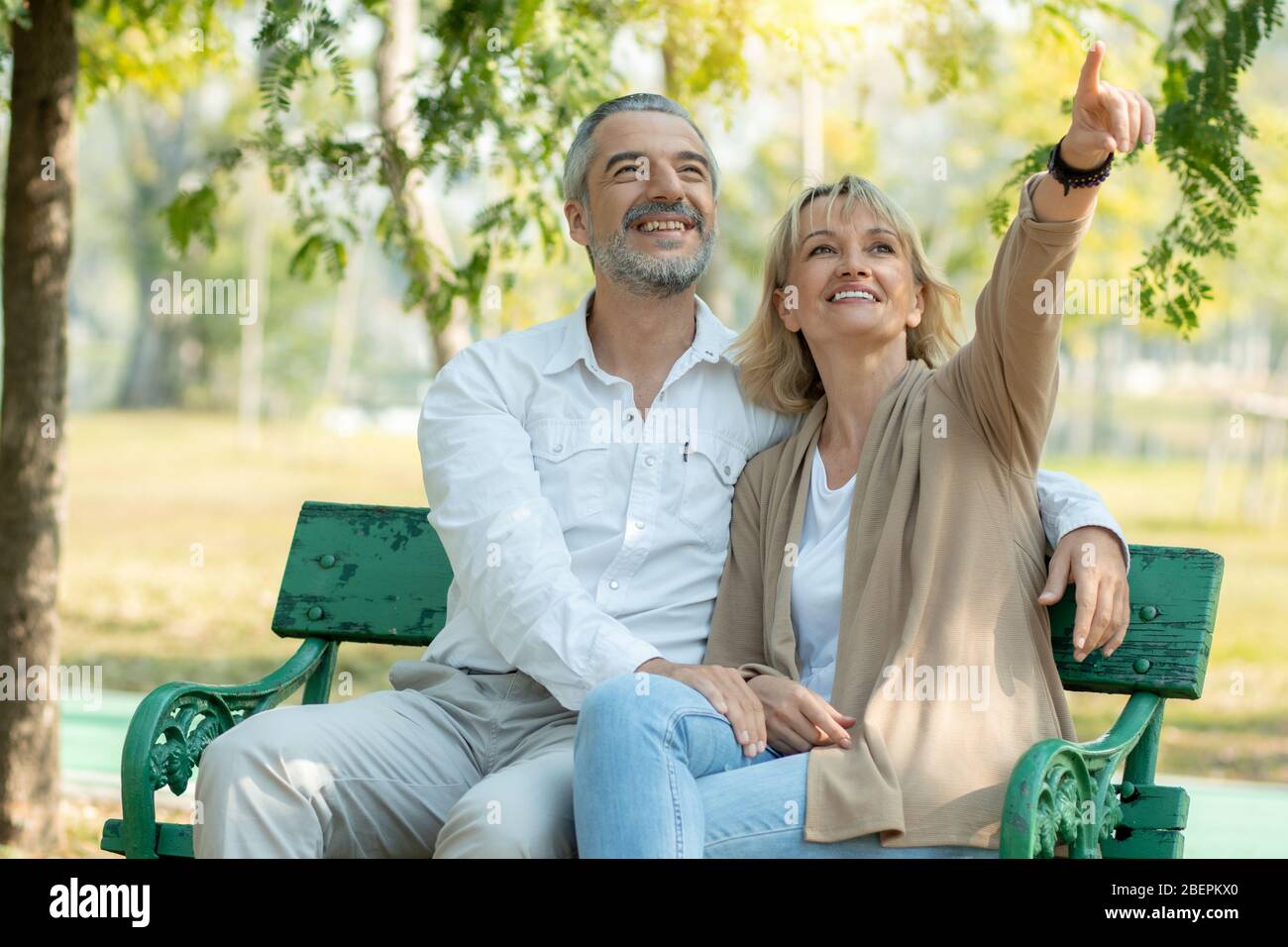 Happy senior couple sit and point to look in park with big smiled Stock Photo