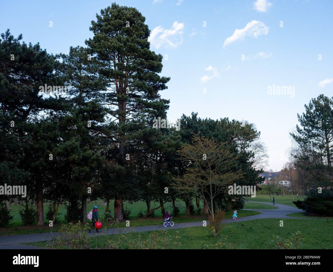 Two children of 2 and 4 years old in a London park on a scooter and bicycle with their mum trailing behind. Roundwood Park, Harlesden, London Stock Photo