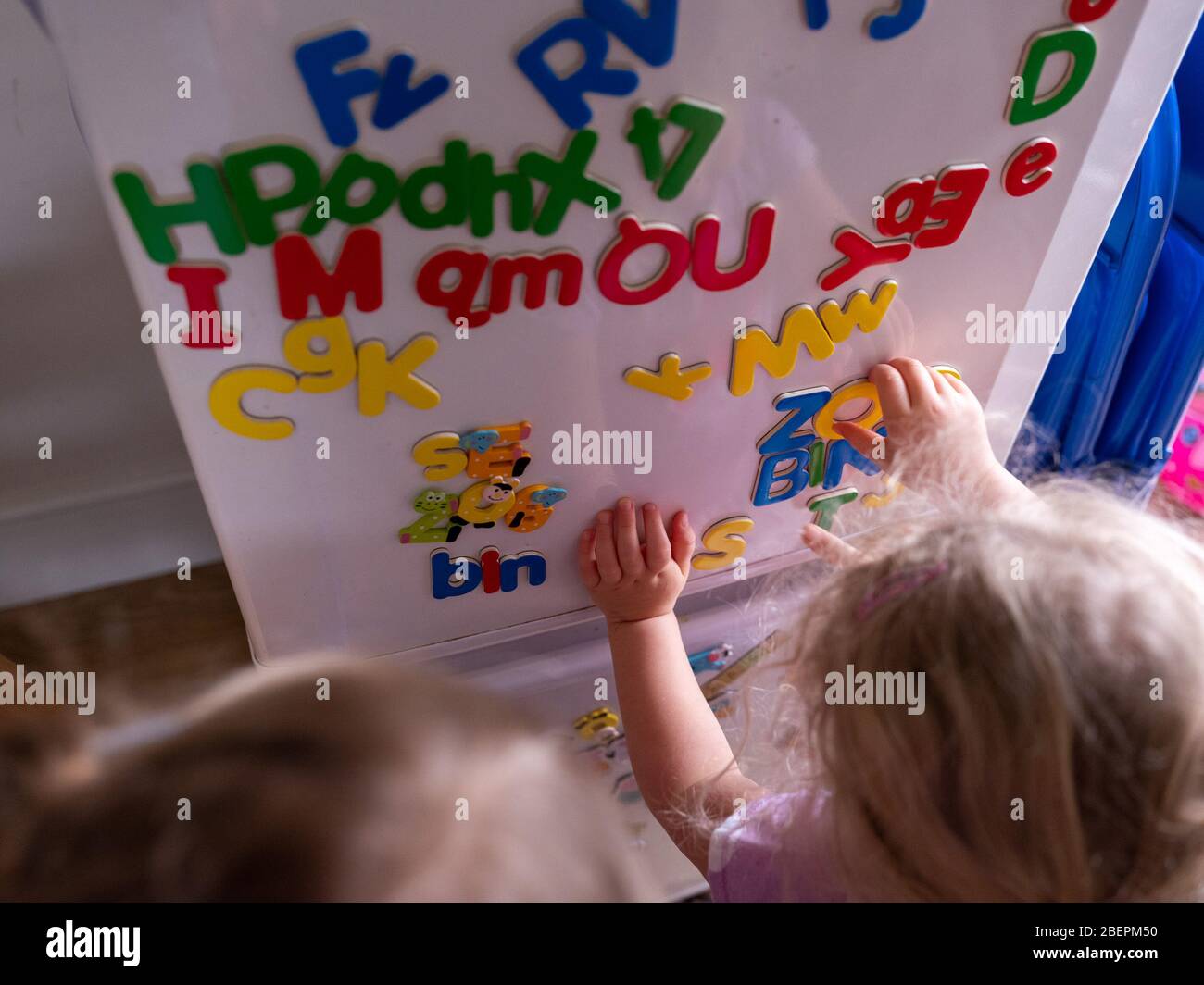 Two children learn the alphabet with magnetic letters one a fridge at home Stock Photo