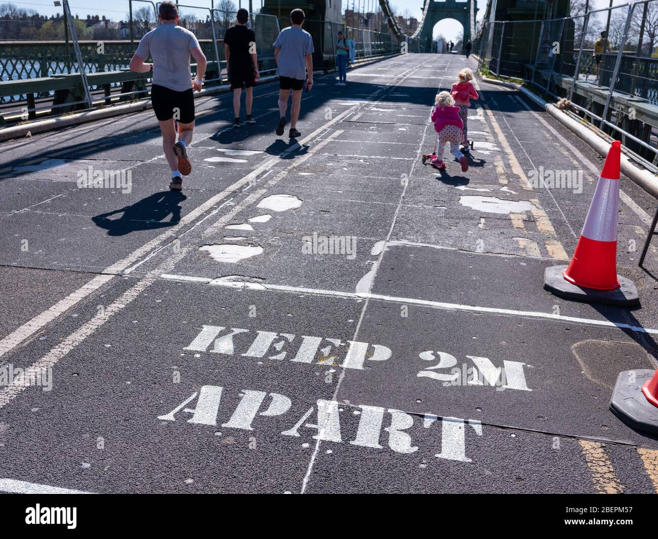A sign painted on the road surface warns pedestrians to keep their distance in order to prevent the Covid 19 virus spreading. Hammersmith Bridge, Lond Stock Photo