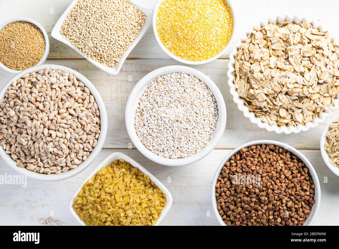 Selection of whole grains in white bowls rice, oats, buckwheat