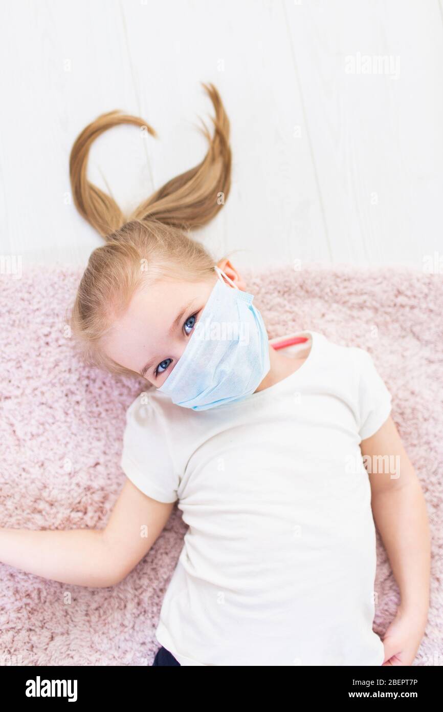 Little blonde girl in protective medical mask on her face lying on a ...