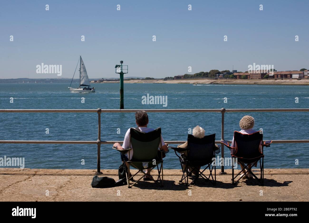 The harbour entrance from the Hot Walls, near the Round Tower, Portsmouth, Hampshire, England, UK: three people sit in a row looking over the Solent Stock Photo