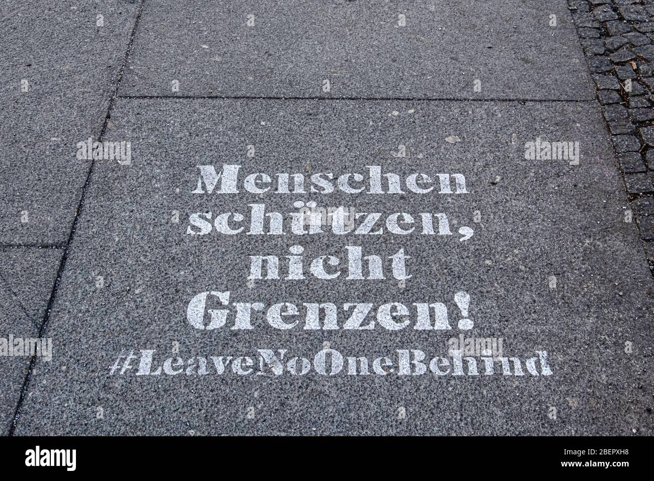 Berlin, Mitte, COVID-19 pandemic.Stencilled message on pavement. Menschen Schutzen nicht grenzen. #Leave No-one behind Stock Photo