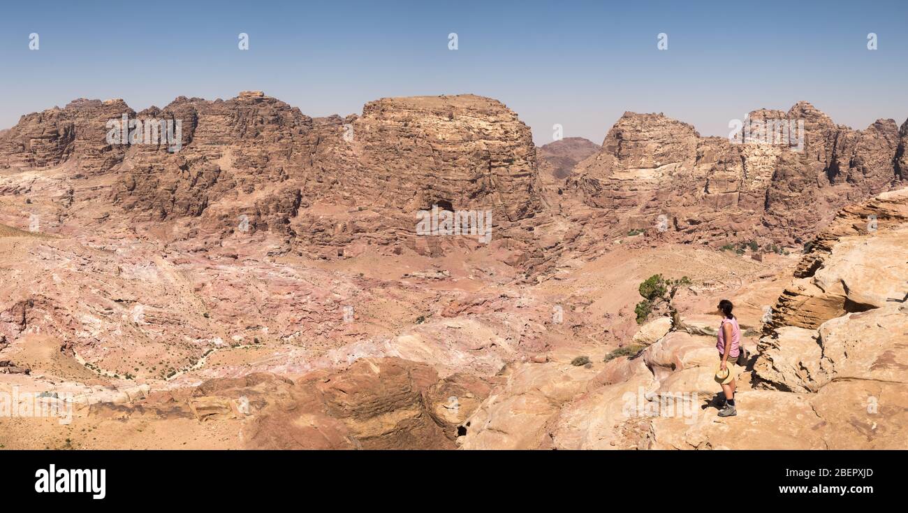 Panoramic view of a female tourist standing at the High Place of Sacrifice looking out at a rocky landscape, Petra, Jordan Stock Photo