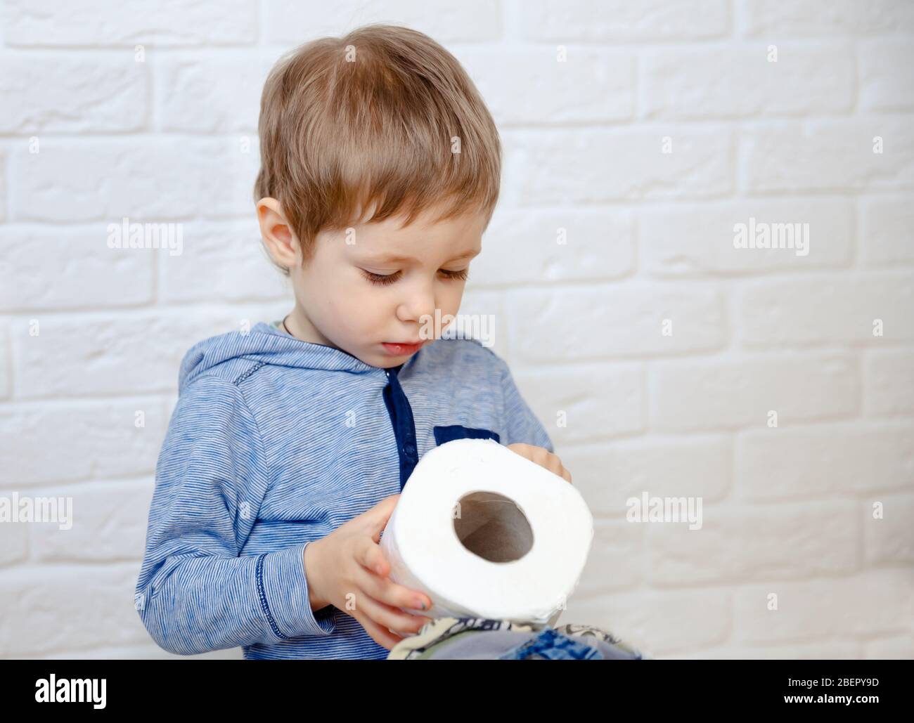 Funny boy sitting on potty chair and playing with toilet paper Stock