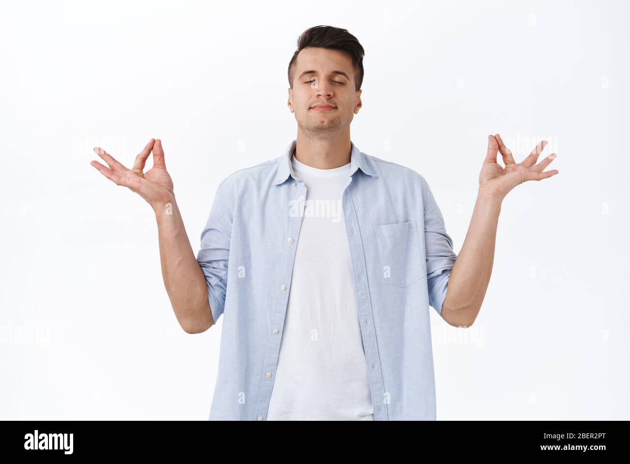 Portrait of relaxed and peaceful smiling handsome man meditating, close eyes breathing deep and carefree spread hands sideways in zen lotus pose Stock Photo