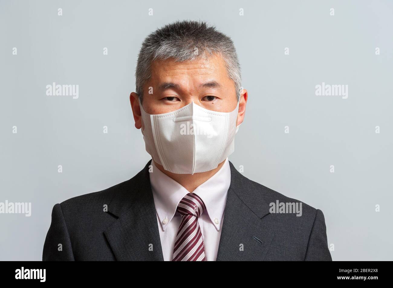 Front view of middle aged Asian man with suit and tie wearing white disposable 3D face mask for protection against novel coronavirus (COVID-19). Stock Photo