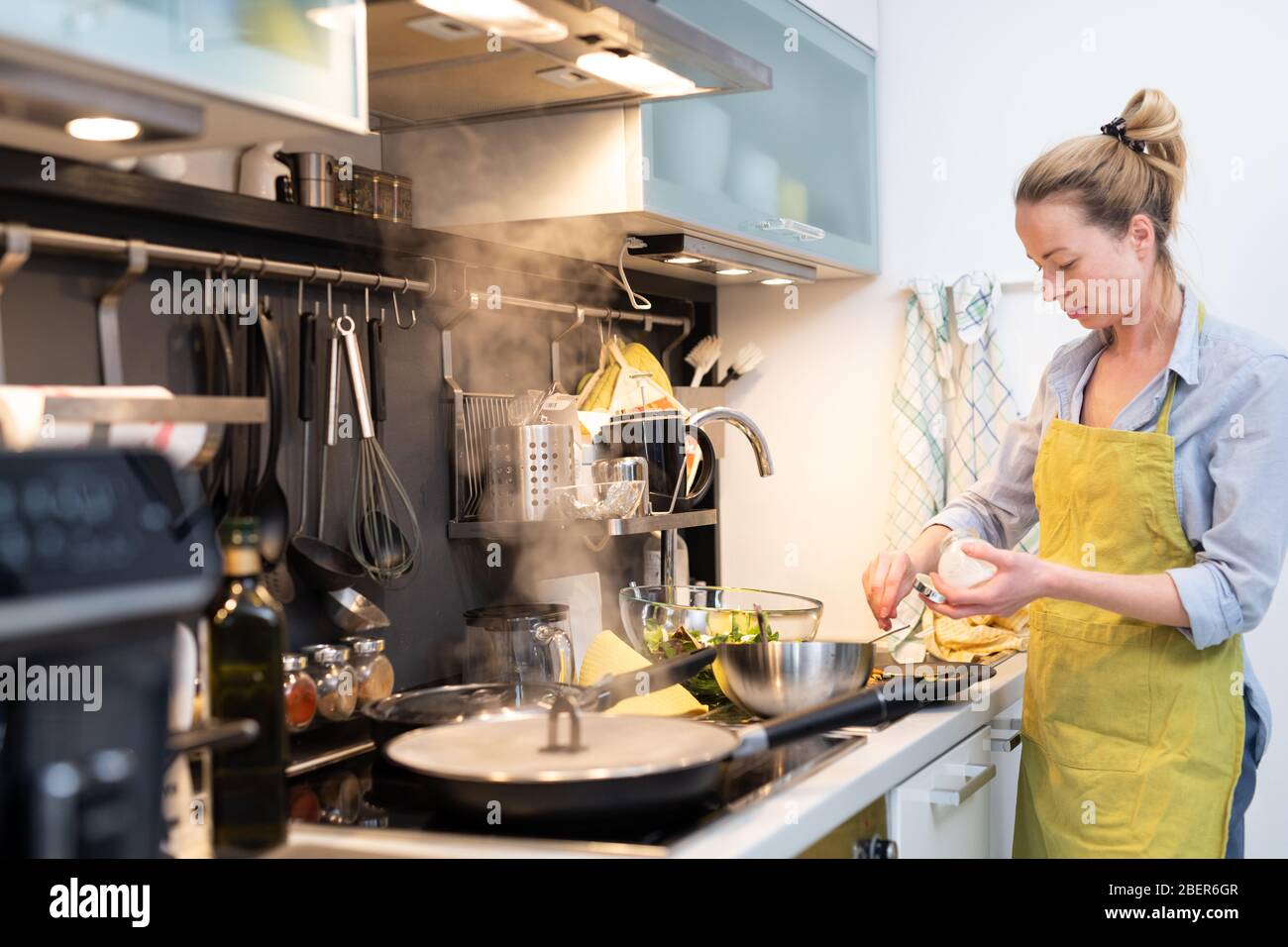 Stay at home housewife woman cooking in kitchen, salting dish in a saucepan, preparing food for family dinner. Stock Photo