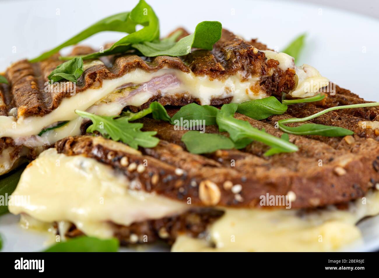 Toasted sandwich with a lot of cheese, ham and green arugula Stock Photo