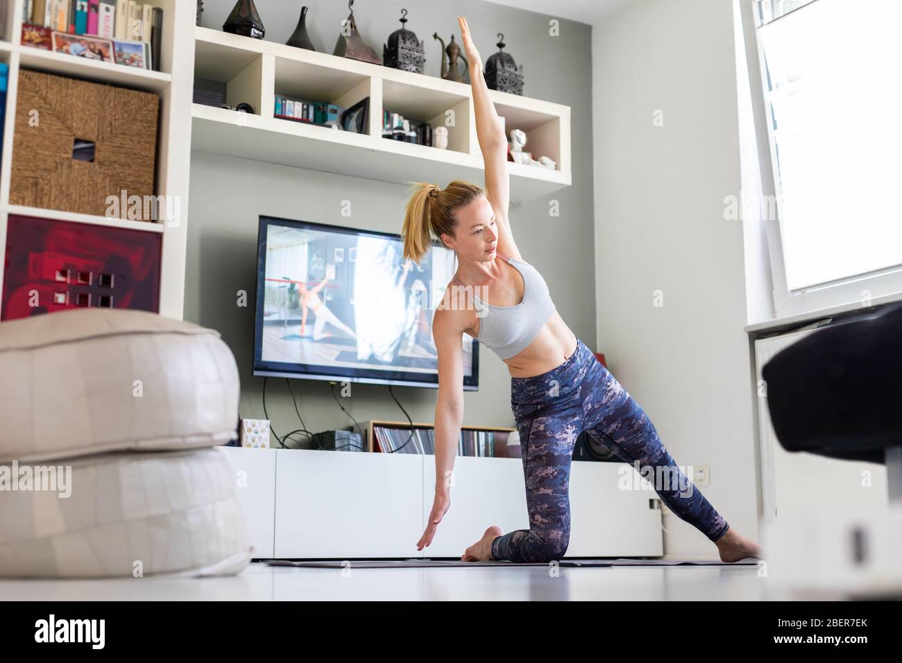 Attractive sporty woman working out at home, doing pilates exercise in front of television in her living room. Social distancing. Stay healthy and Stock Photo