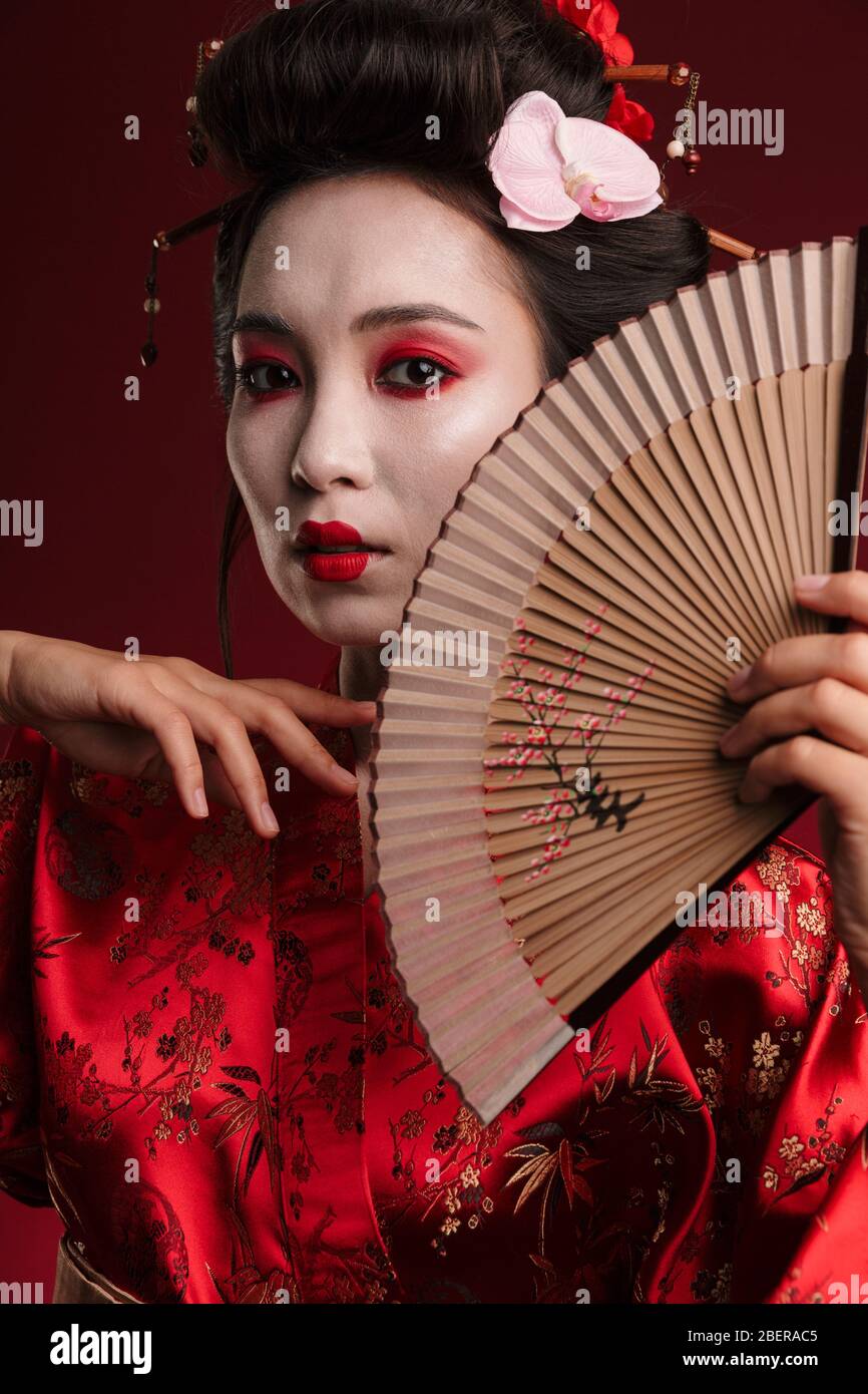 Image of young geisha woman in traditional japanese kimono holding wooden  hand fan isolated over red background Stock Photo - Alamy
