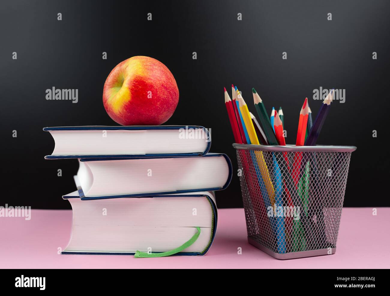 education concept, fresh apple on stack of books next to pencil cup with colored pencils Stock Photo