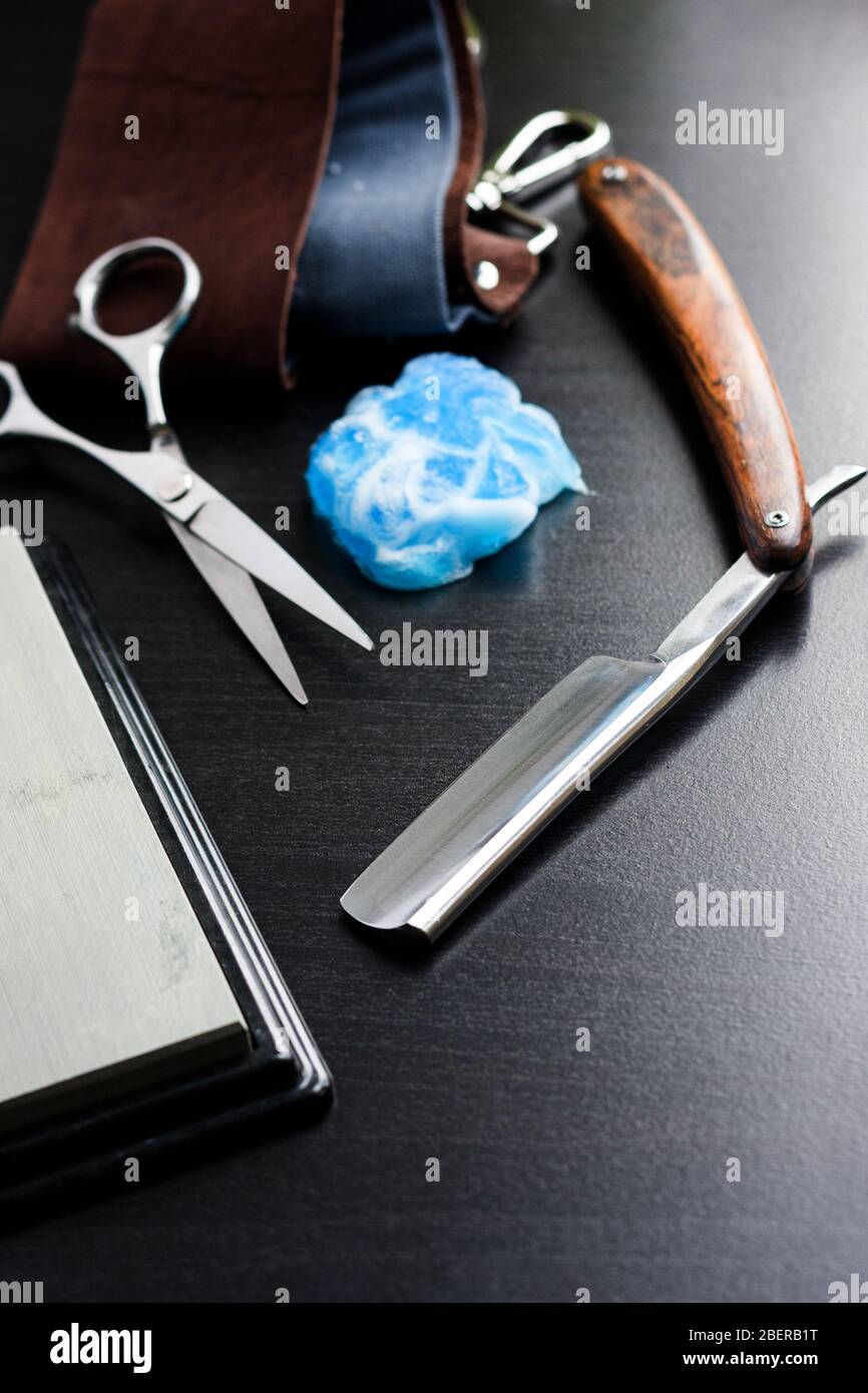 Straight razor, shaving foam, leather tool and scissors on black wooden