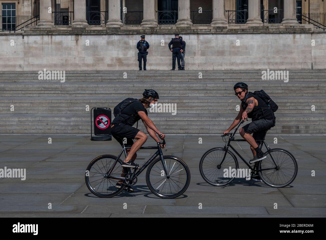 London, UK. 15th Apr, 2020. Two men on bikes film each other in a fairly quiet Trafalgar Square, while out on their daily exercise watched by two PCSOs- The 'lockdown' continues in London because of the Coronavirus (Covid 19) outbreak. Credit: Guy Bell/Alamy Live News Stock Photo