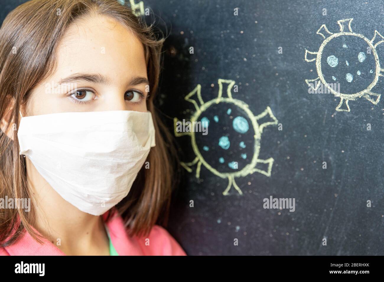 Sad girl with mask at home together drawing a coronavirus on a blackboard Stock Photo